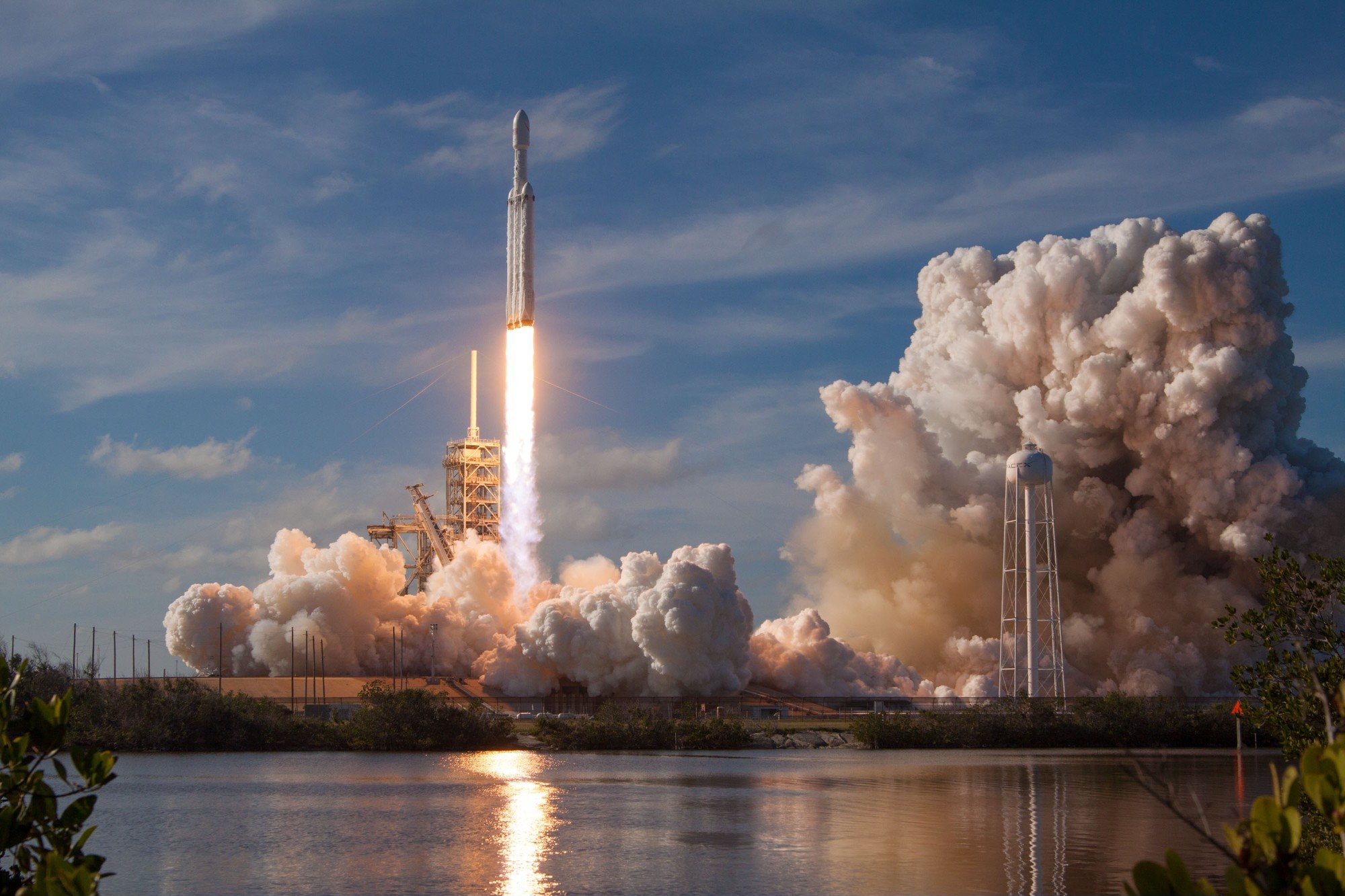 Despegue del Falcon Heavy entre nubes de vapor, reflejado en el agua