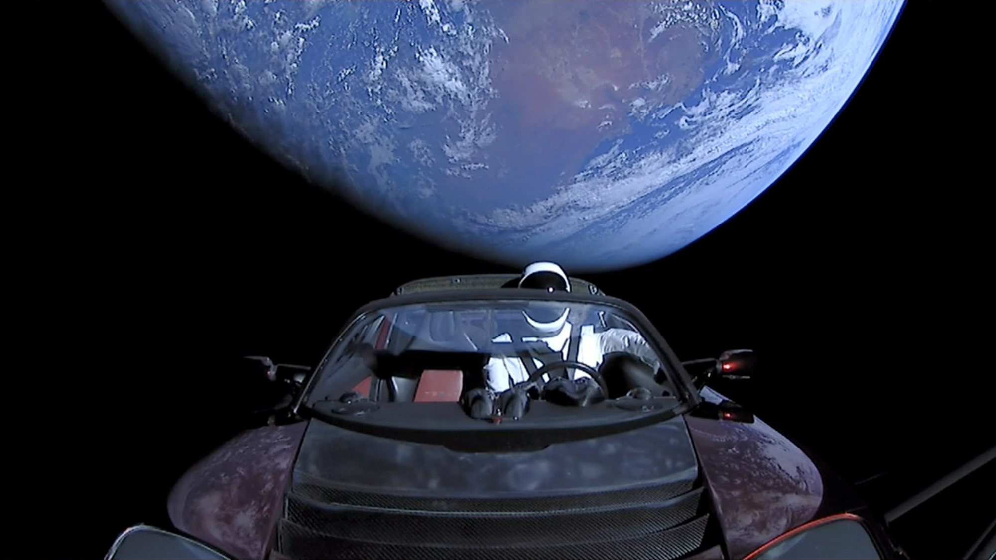 Un Tesla Roadster con el maniquí Starman al volante, en el espacio y con la Tierra de fondo